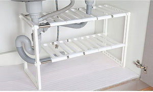 White under-sink storage shelf with pipes and a drain in a bathroom setting.